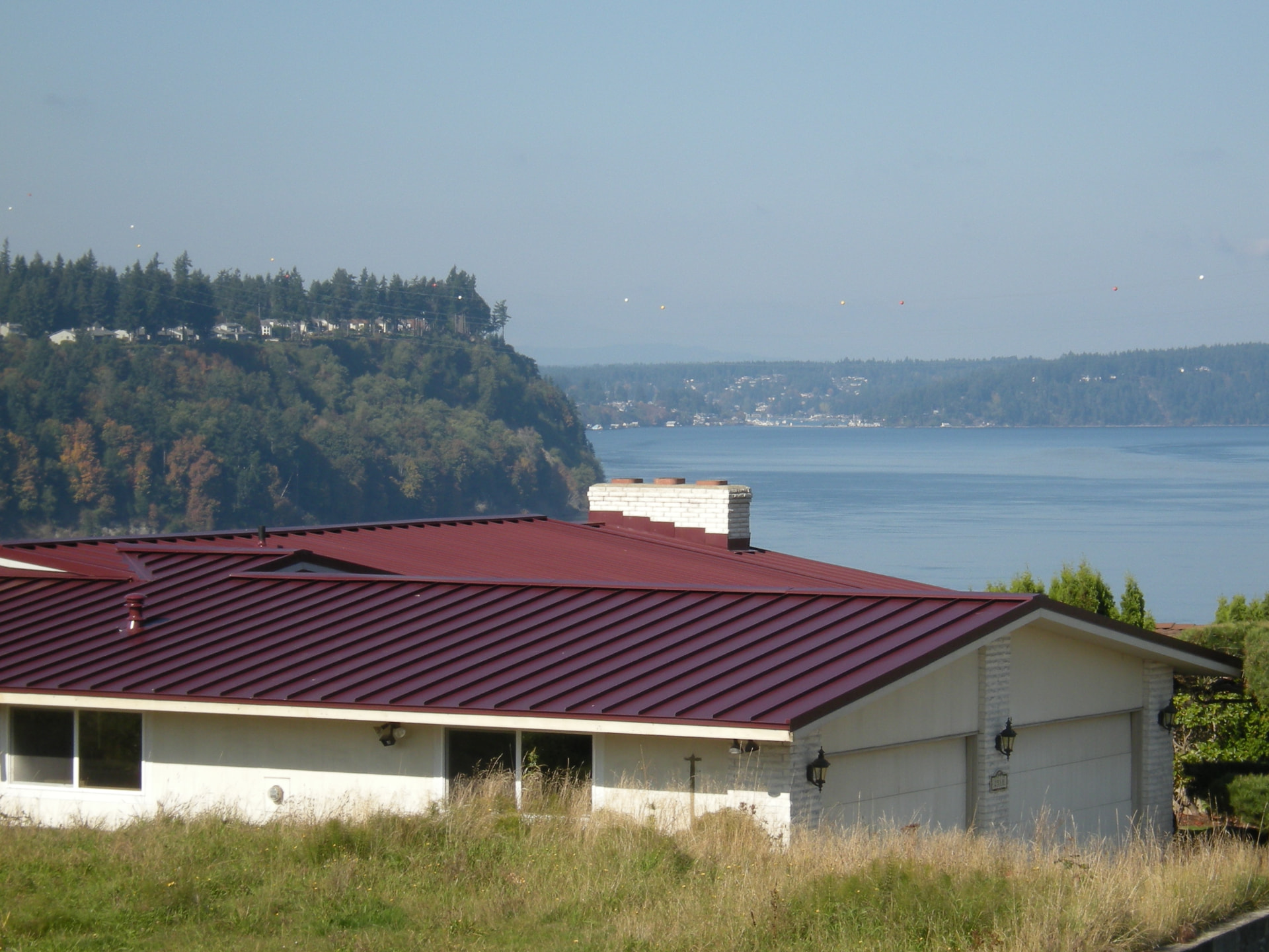 Deep red metal roof with waterfront view after replacement by DHT Construction & Roofing