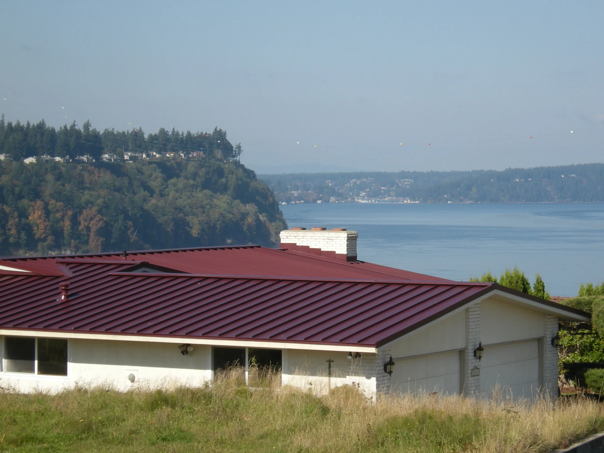 Deep red metal roof with waterfront view after replacement by DHT Construction & Roofing